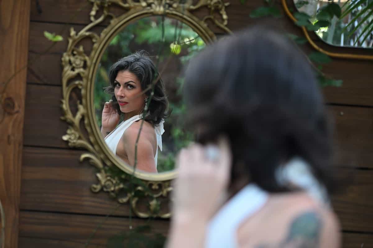 Elegant woman in white dress gazing into a vintage ornate mirror outdoors representing the spiritual traditions and cultural meanings associated with mirror dreams