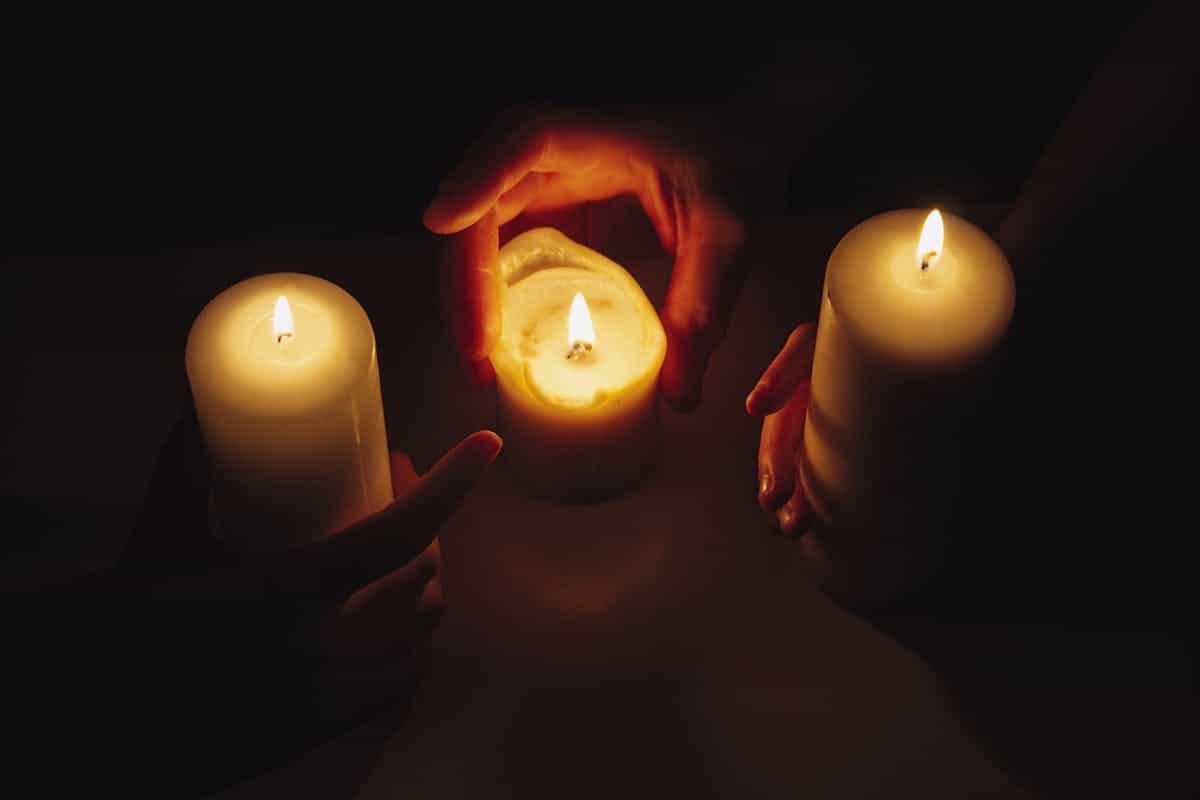 Hands cupping small lit candles in a dark intimate meditation setting
