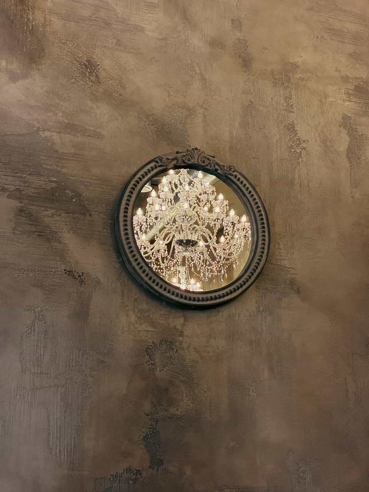Chandelier reflection in an ornate round interior mirror Round decorative mirror reflecting a crystal chandelier on textured wall suggesting inner light and reflection symbolism