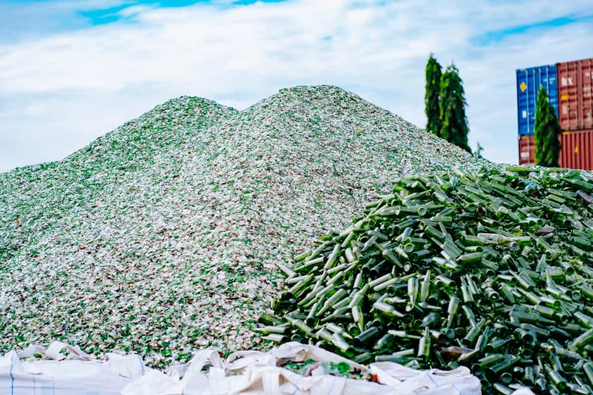 Industrial piles of recycled glass bottles and shards under a bright sky at a processing facility