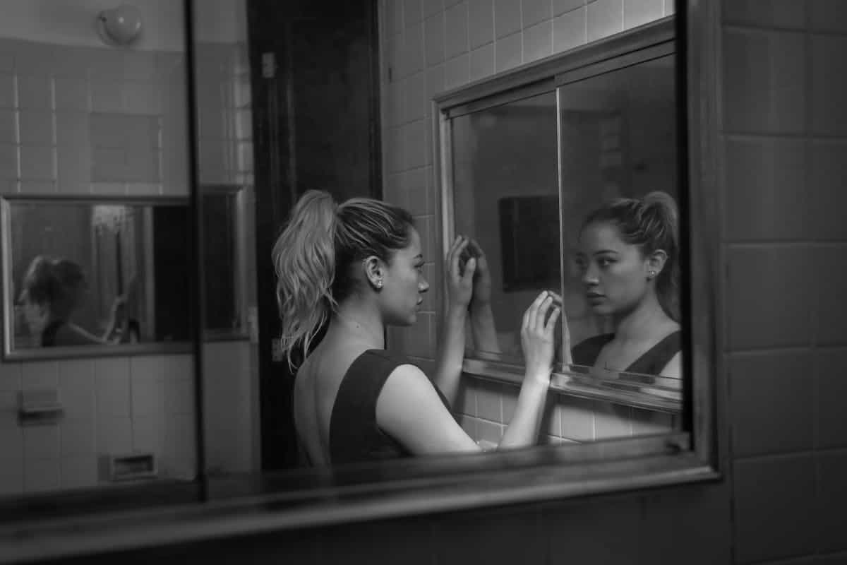 Woman facing her bathroom mirror reflection in monochrome Black and white photograph of a woman gazing at her reflection in a bathroom mirror for Jungian shadow and identity dream themes