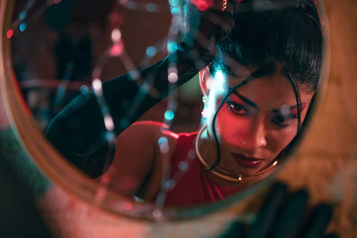 A dramatic portrait of a woman looking into a cracked mirror highlighting her intense gaze and the tension of fractured self-reflection