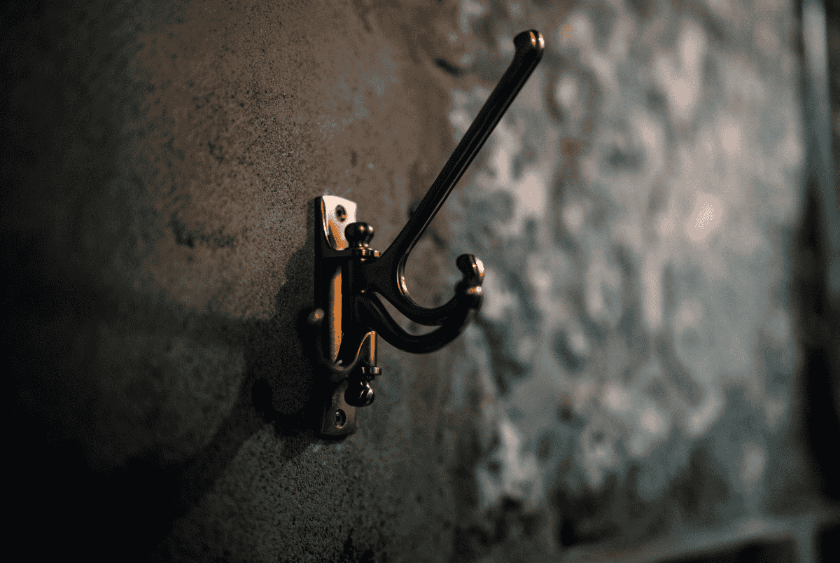Brass coat hook close-up illustrating hook quality in an entryway mirror with hooks Close-up of a brass coat hook mounted on a textured wall, showing hook quality to look for in an entryway mirror with hooks