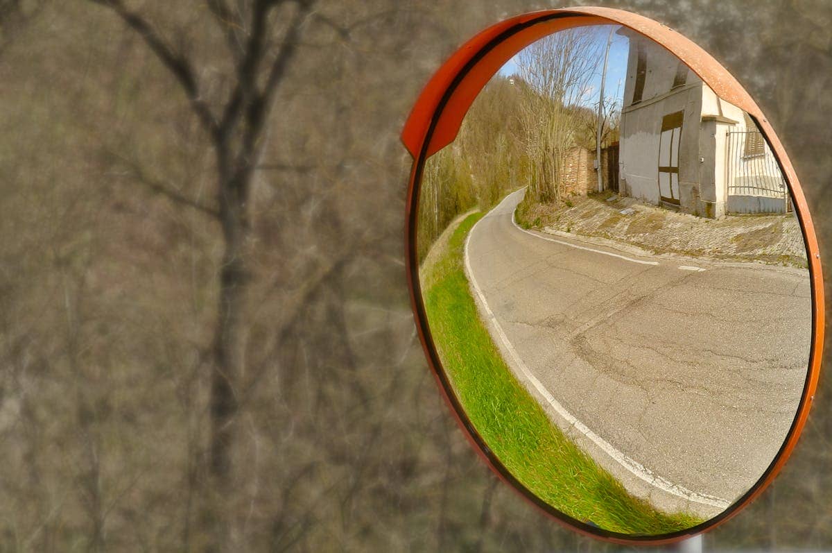 Convex mirror showing a wide-angle view of a curved rural road demonstrating how convex surfaces always produce diminished virtual images with a broader field of view than plane mirrors