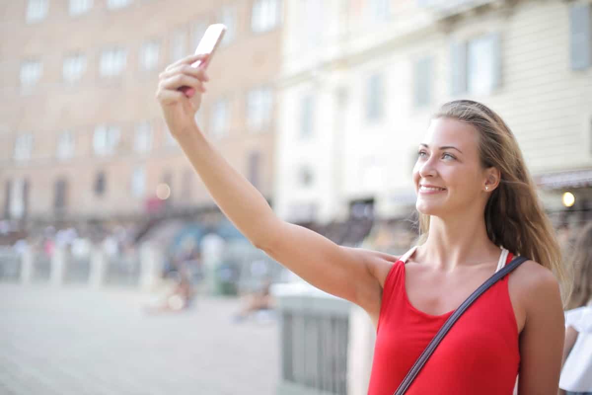 Young woman holding smartphone up for selfie in natural outdoor light suggesting curated self image