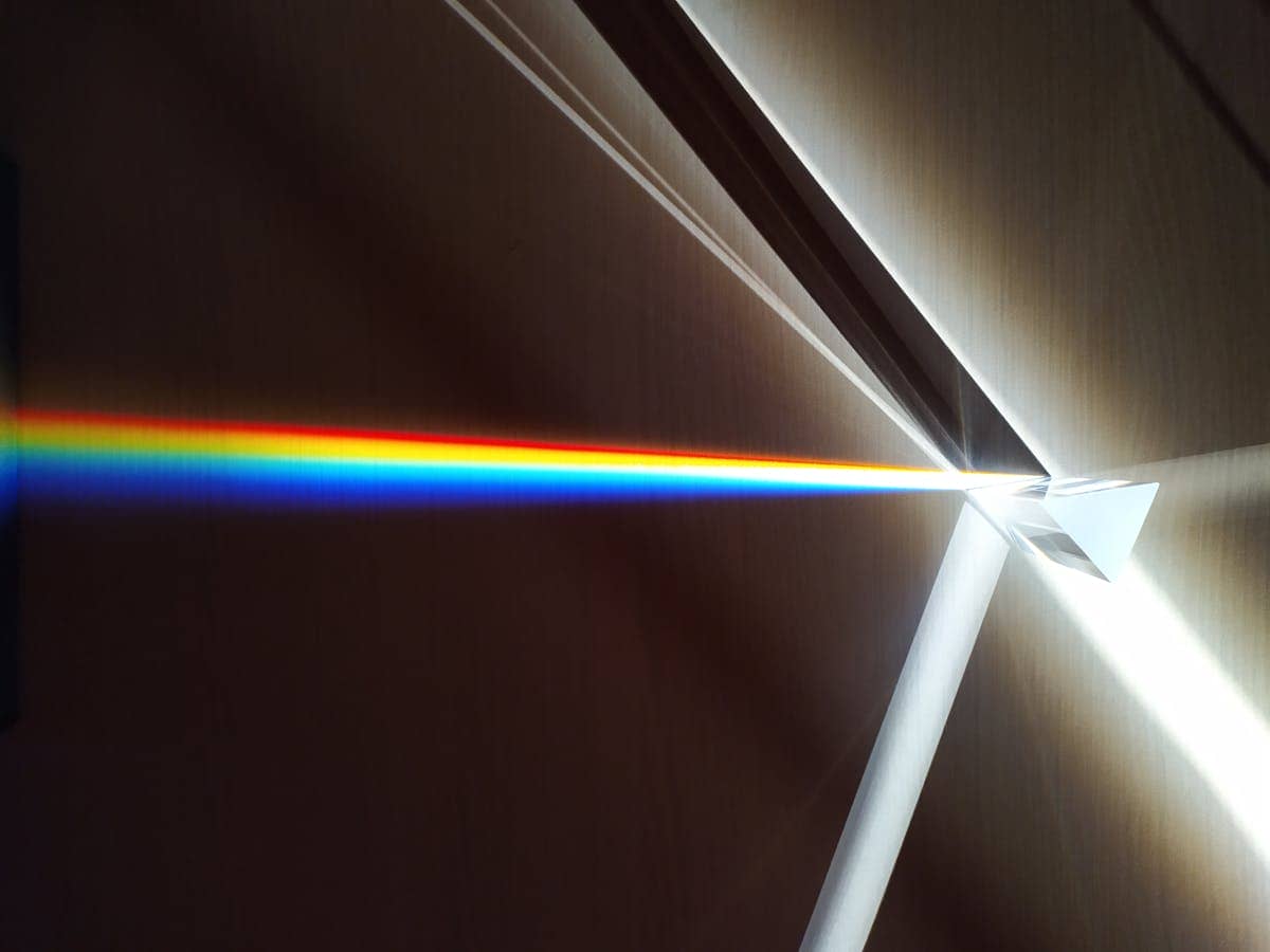 Colorful light spectrum refracted through a glass triangular prism illustrating the optics of light wavelengths from 380 nm violet to 700 nm red used in mirror and lens calculations