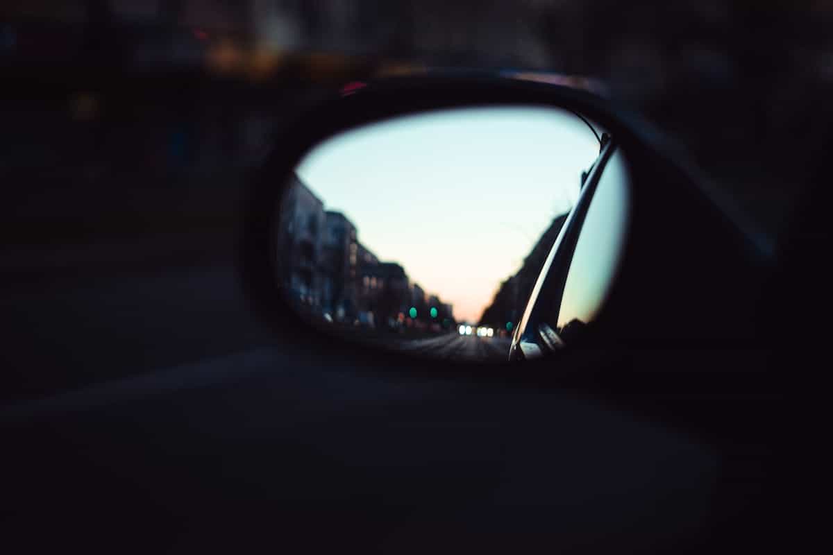 Twilight city avenue mirrored inside automotive rear surface illustrating doubled worlds symbolism