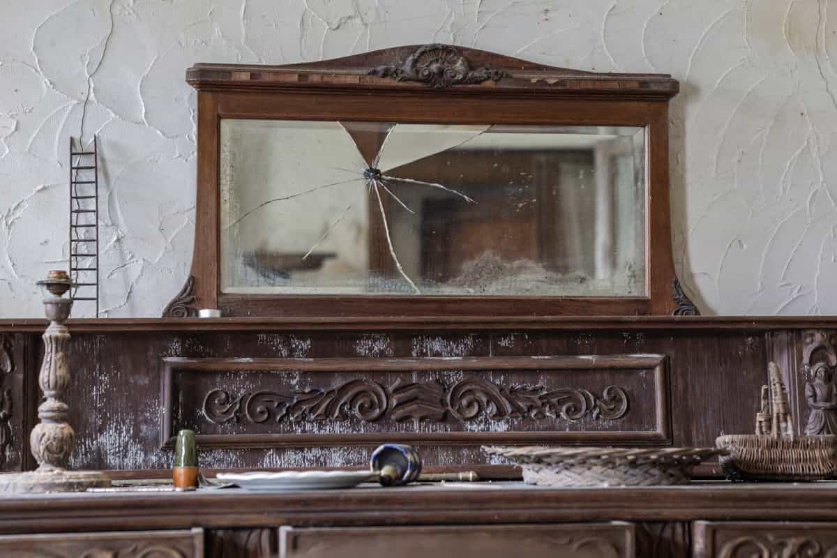 Antique cracked mirror on rustic sideboard evoking mirror superstition history and folk belief Antique wooden sideboard with cracked mirror in rustic interior linking folk beliefs and age of mirrors