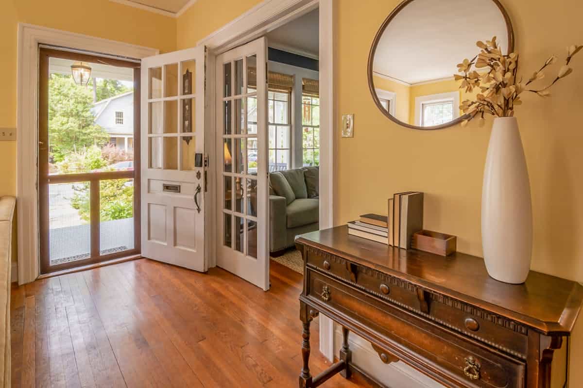 Sunlit entryway with wooden dresser ornate mirror and decorative branch vase illustrating feng shui mirror entryway placement for welcoming Chi
