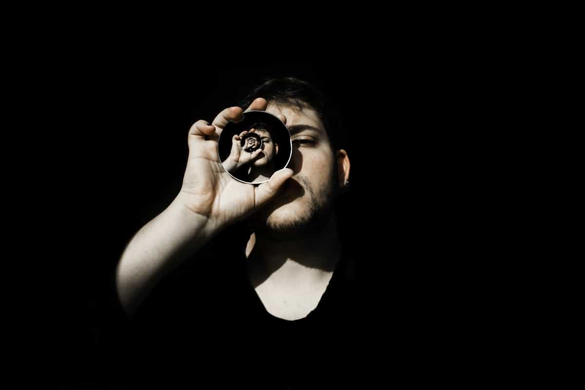 Creative portrait holding small mirror against deep black backdrop suggesting staged portal symbolism