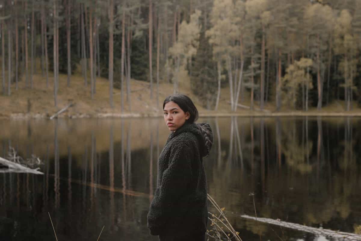 Woman standing at lakeshore looking across calm water toward distant mountains contemplative mood