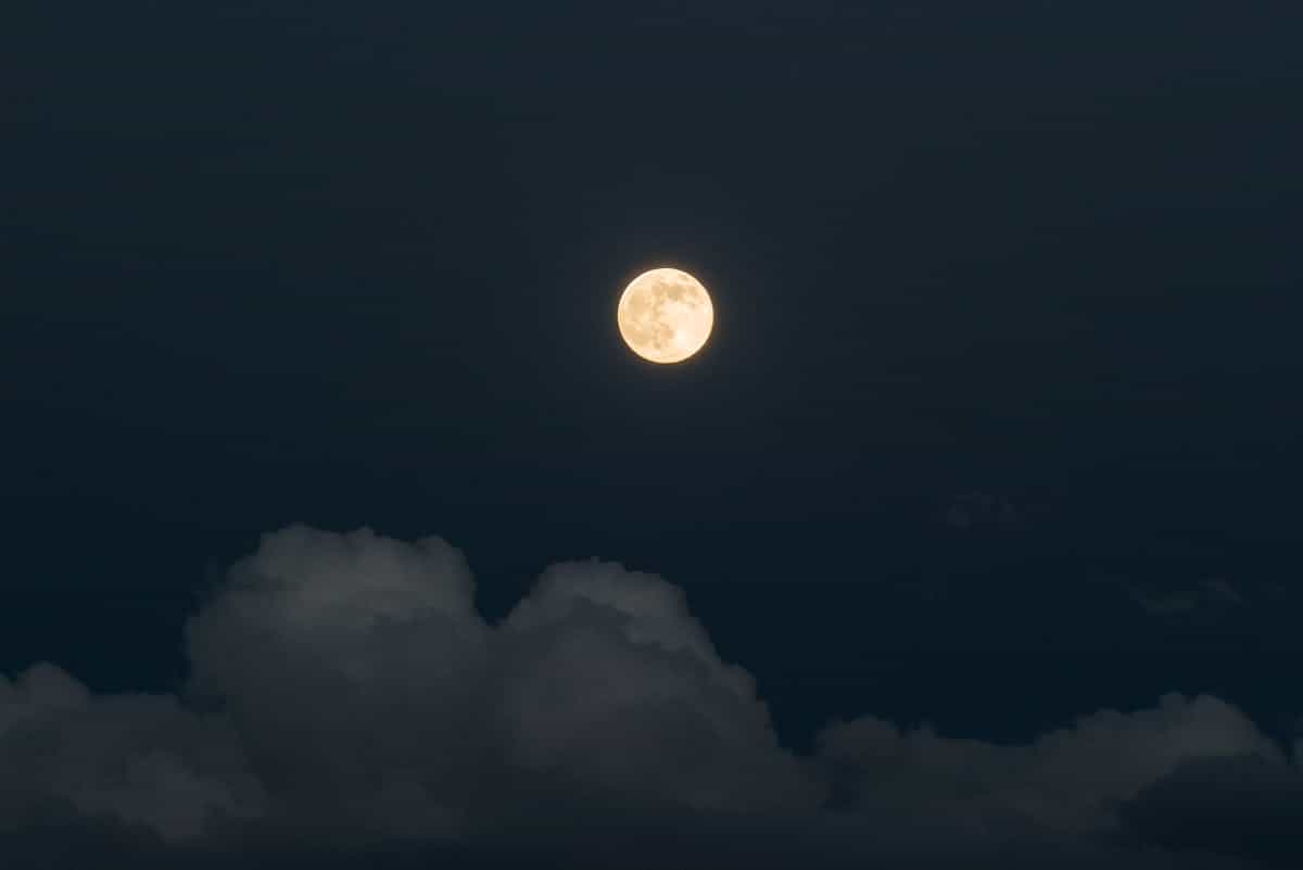 Full moon glowing above thin clouds in a deep blue night sky