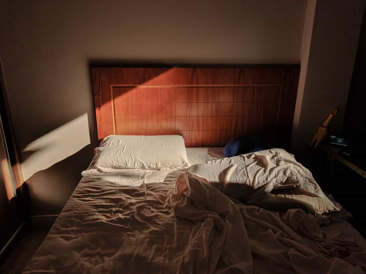 Bed with a wooden headboard illustrating how to orient the bed by feng shui sleeping direction Sunlit bed with a wooden headboard in a warm bedroom, illustrating orienting the bed for feng shui sleeping direction
