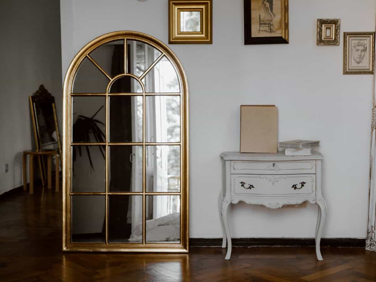 Vintage-style interior with a gold arched mirror above a console, illustrating round and arched living room mirrors