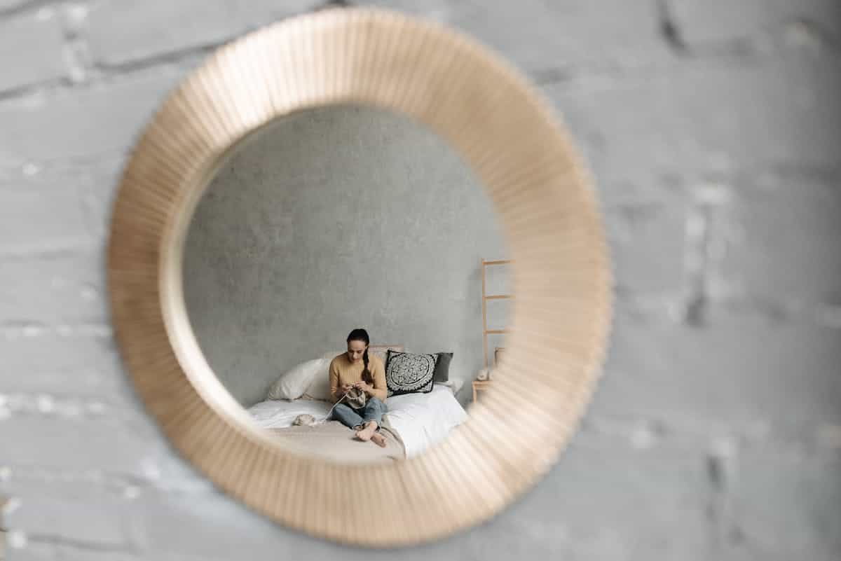 Person resting on a bed reflected in a round wall mirror, showing why a mirror over a nightstand should not reflect the bed