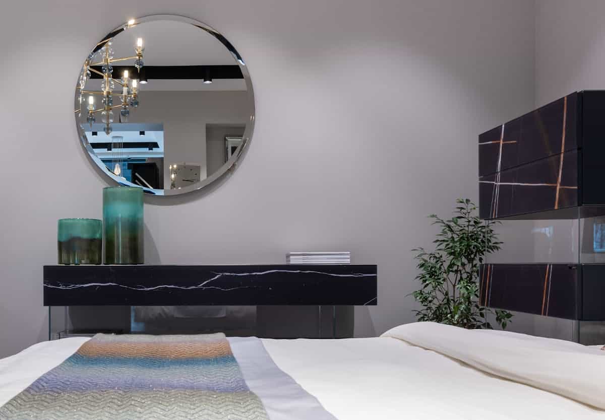 Round mirror mounted on the wall above a bed showing the best mirror shape above a bed