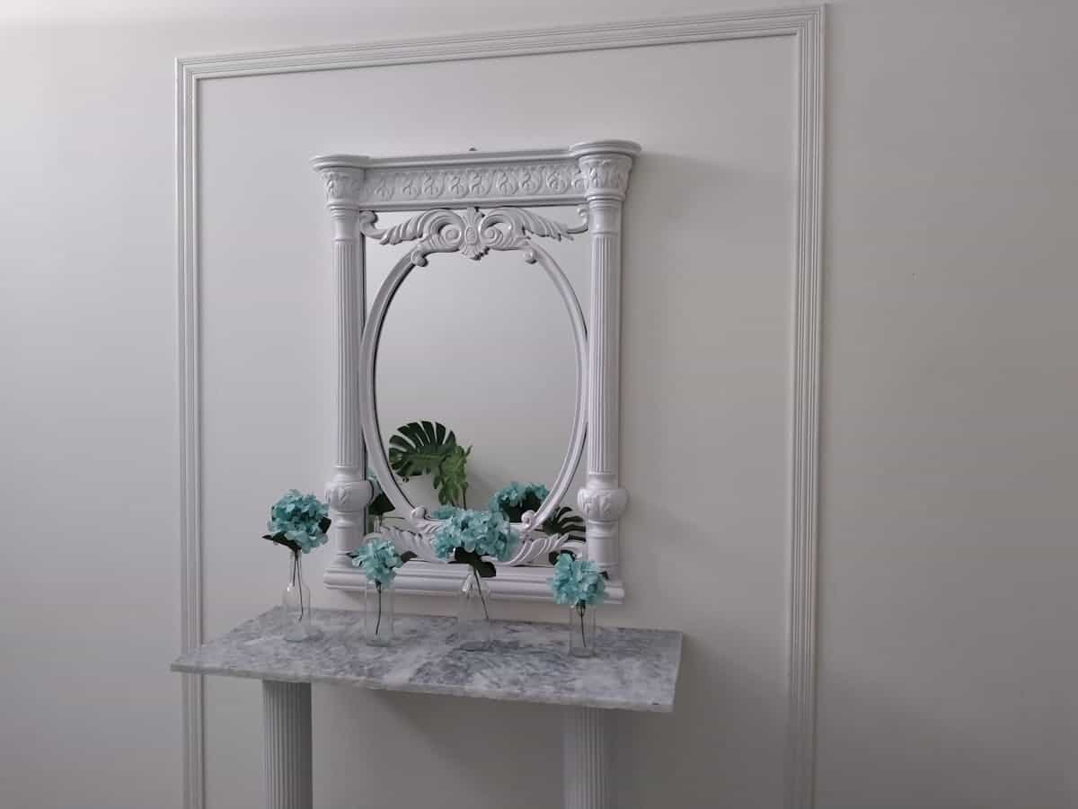 Sophisticated white wall with a decorative arched mirror and a floral arrangement, illustrating arched mirror wall ideas.
