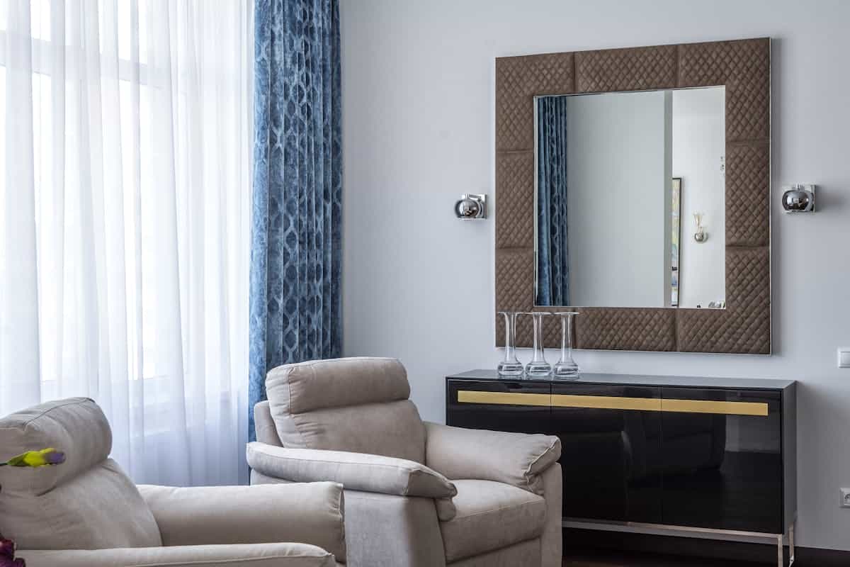 Modern living room with armchairs and a large square framed mirror, illustrating mirror frame and shape choices