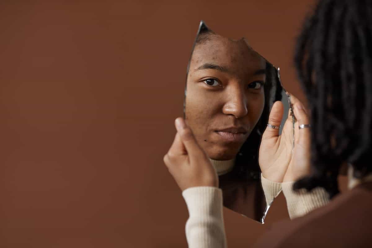 A woman holding and looking into a broken mirror reflecting on self image and fractured identity representing literary symbolism of shattered self-perception