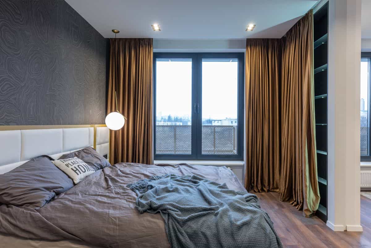 Calm bedroom with a soft bed beside a window dressed with curtains, illustrating heavy curtains as a feng shui cure