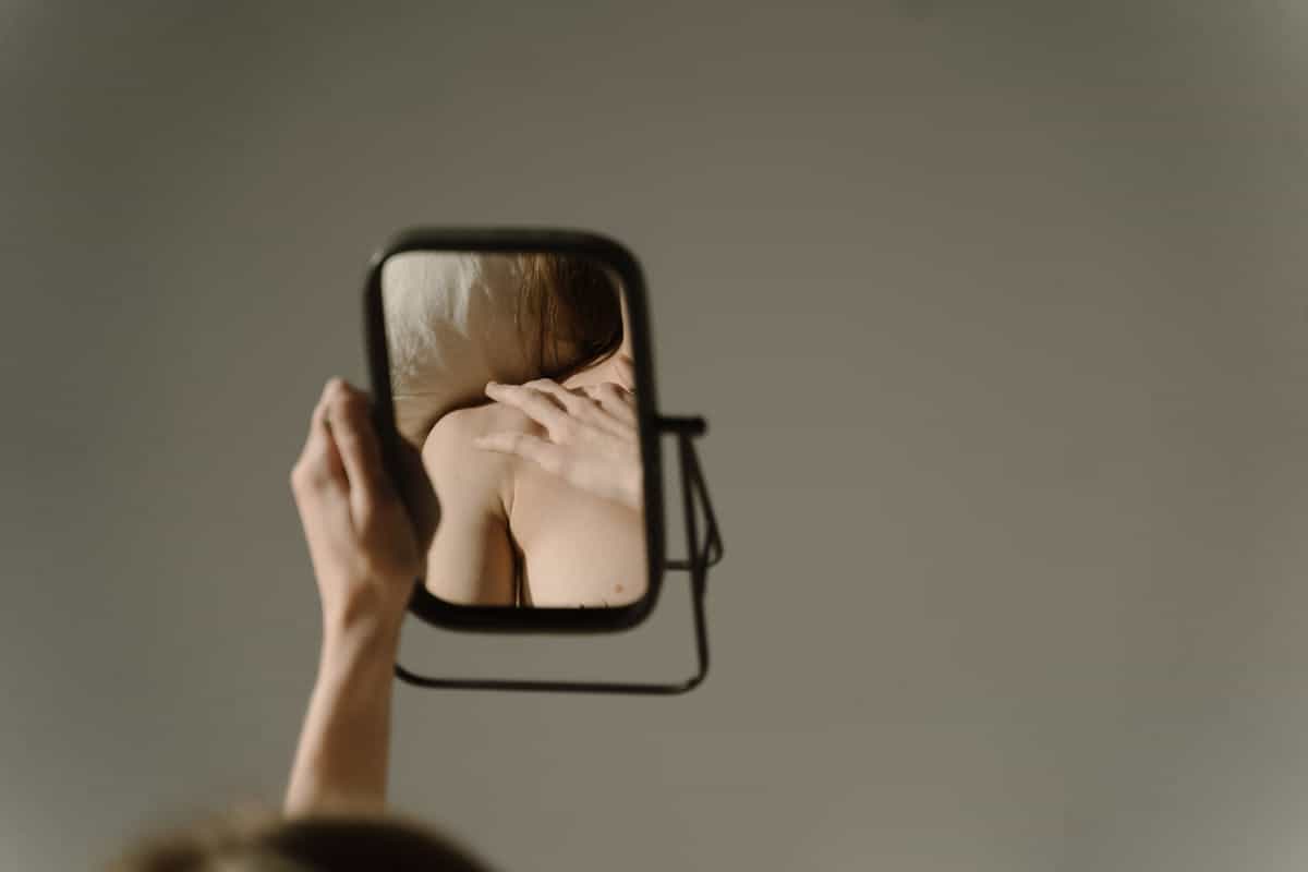 Artistic close-up of thoughtful woman studying her reflection aligning with optics questions about mirrored perception