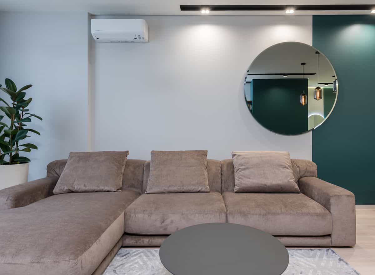 Round mirror hanging on the wall above a comfortable sofa in a modern living room, illustrating a mirror over a sofa.