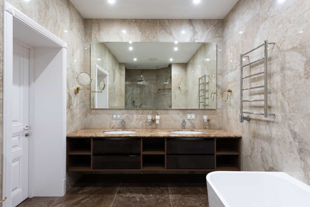 Hands adjusting a framed wall mirror over a sink in a small bathroom