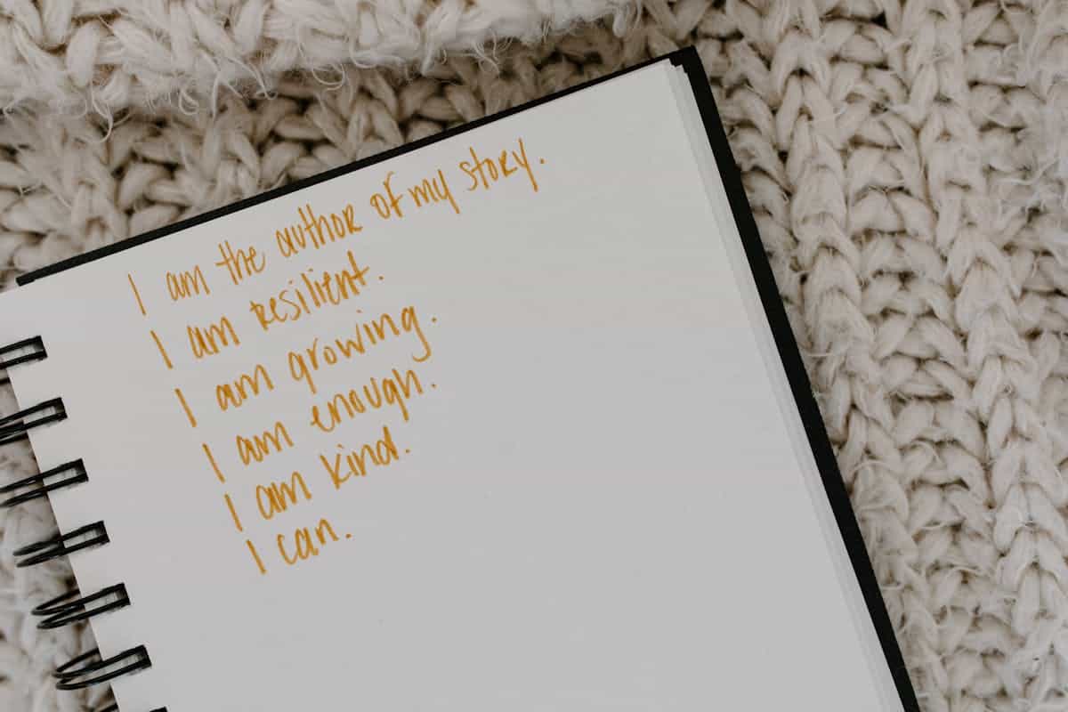 A notebook open to a page filled with handwritten affirmations and personal growth statements on a knitted fabric surface