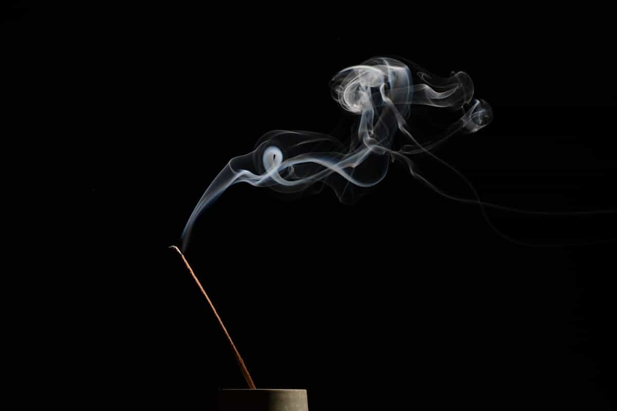 Incense stick releasing soft smoke in soft warm light for home cleansing ritual atmosphere