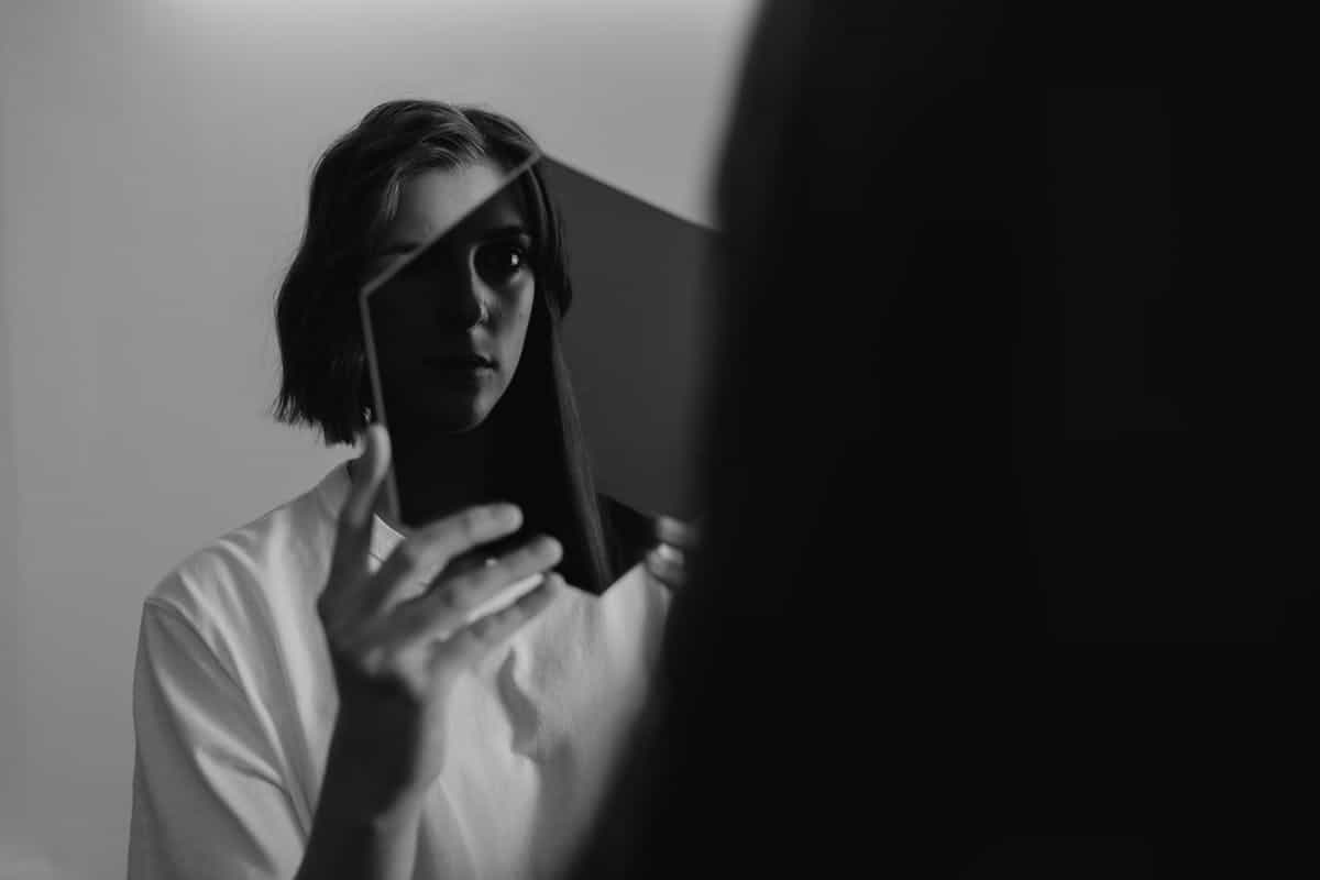 Monochrome image of a woman reflecting on herself in a mirror evoking self-awareness and mirror psychology