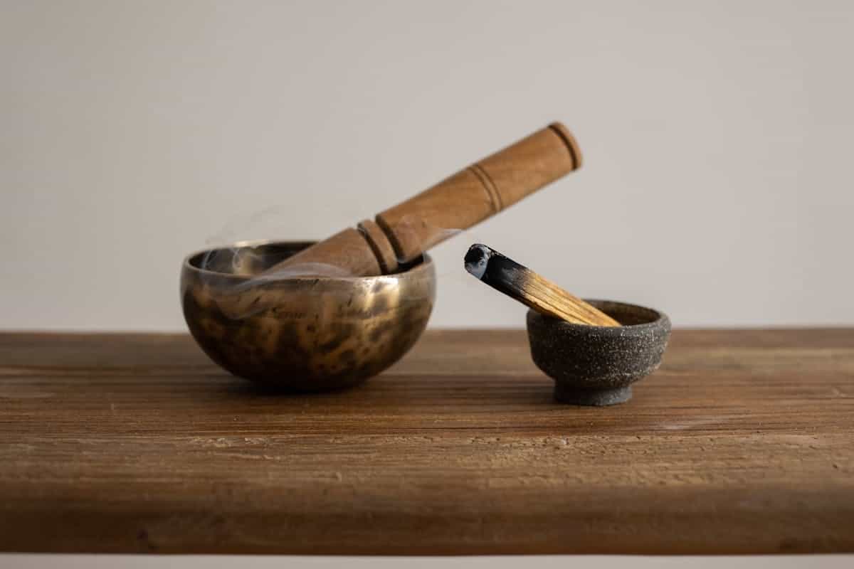 Singing bowl and burning incense on a wooden table evoking ancient ritual and the historical practice of water scrying and seeking visions in reflective surfaces