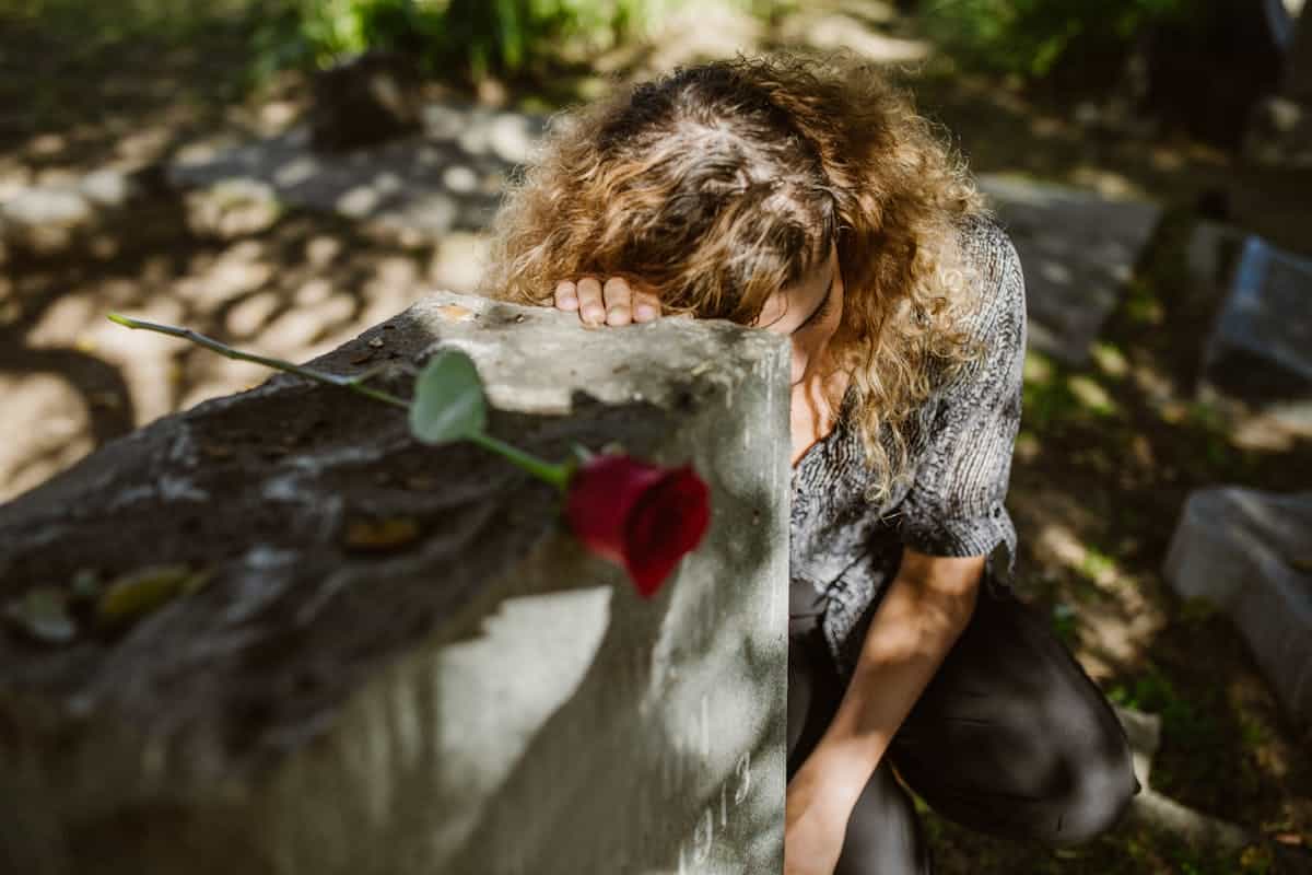 A woman kneeling in grief at a graveside in a cemetery representing the experience of dreaming about deceased loved ones appearing in mirror reflections
