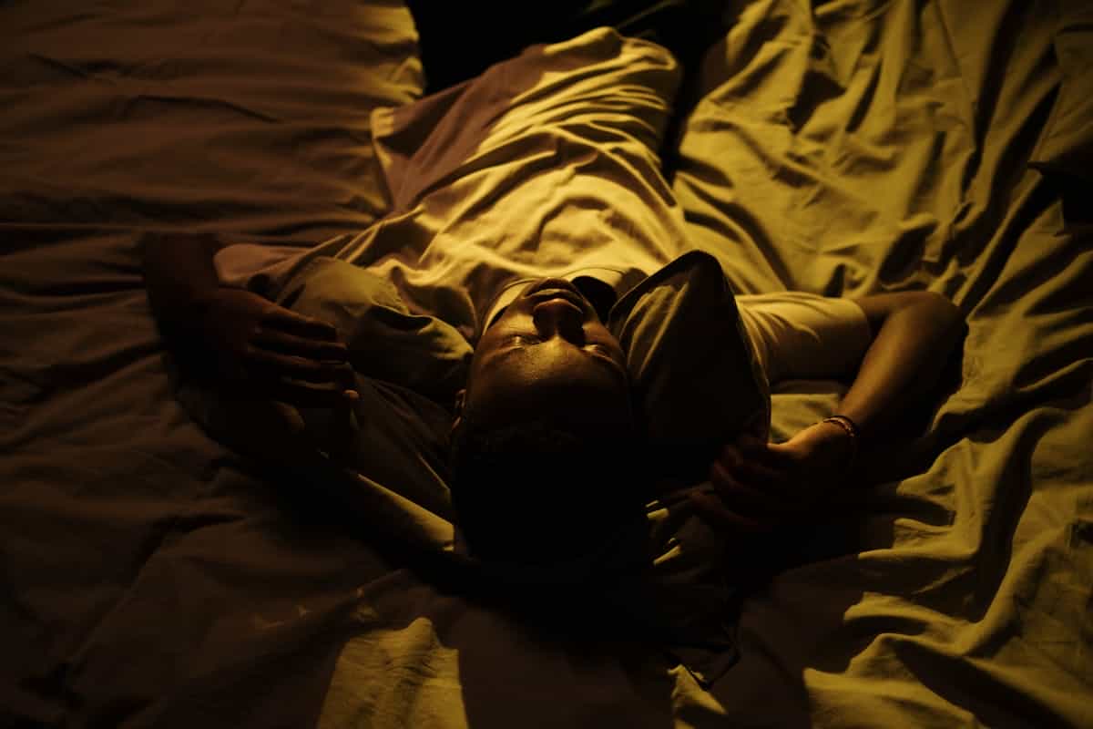 A man lies in bed at night, struggling with insomnia in a dimly lit bedroom