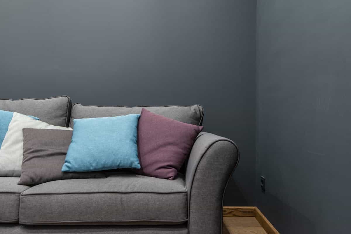 Sofa against a solid wall illustrating the most important feng shui sofa placement rule Grey sofa with cushions placed against a wall in a bright living room, illustrating the main feng shui sofa placement rule