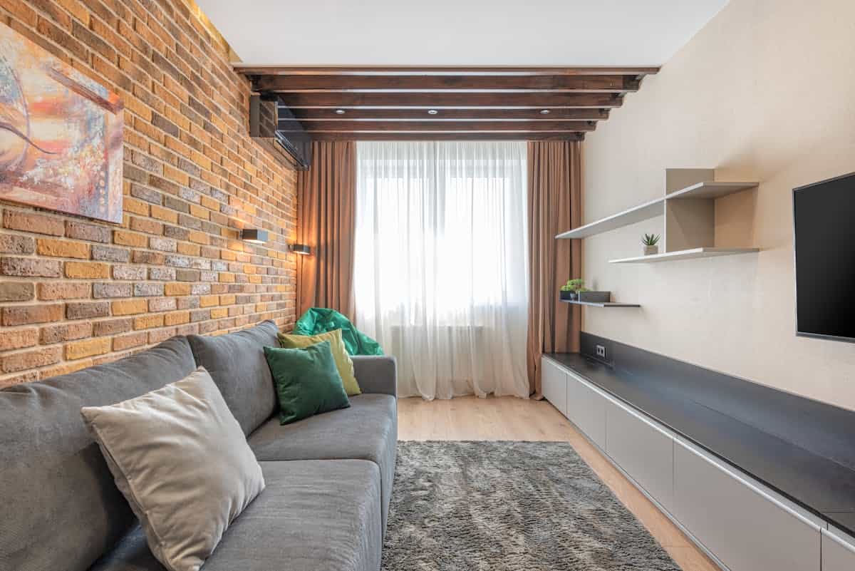 Living room with an exposed brick accent wall illustrating brick and stone accent wall ideas Living room with a rustic exposed brick wall and a gray sofa, illustrating a brick accent wall