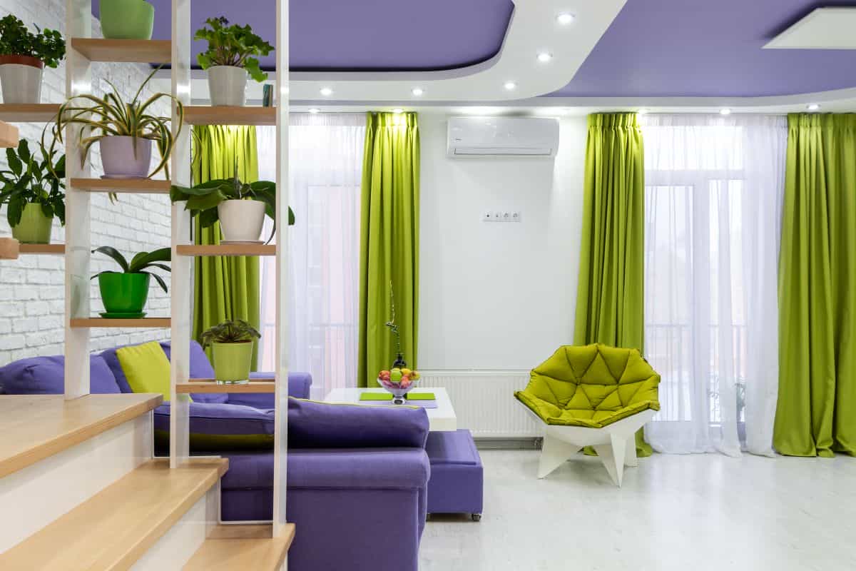 Living room with purple and green accents illustrating feng shui prosperity and wealth-corner colors Bright living room with a purple sofa, green armchair and plants, illustrating feng shui prosperity colors