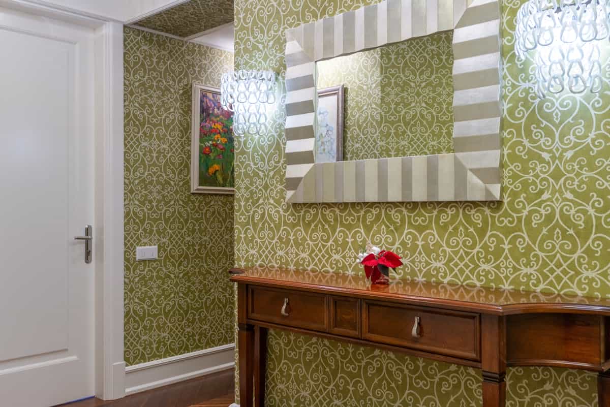 Hallway console and mirror hung at eye level showing correct hallway mirror height Sophisticated hallway with ornate wallpaper, a wooden console, and a mirror at eye level