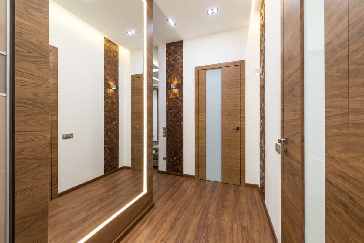 Contemporary narrow hallway illustrating the best mirror shapes and frames for tight spaces Sleek contemporary hallway with wooden elements and warm light, showing mirror shapes for a narrow hallway