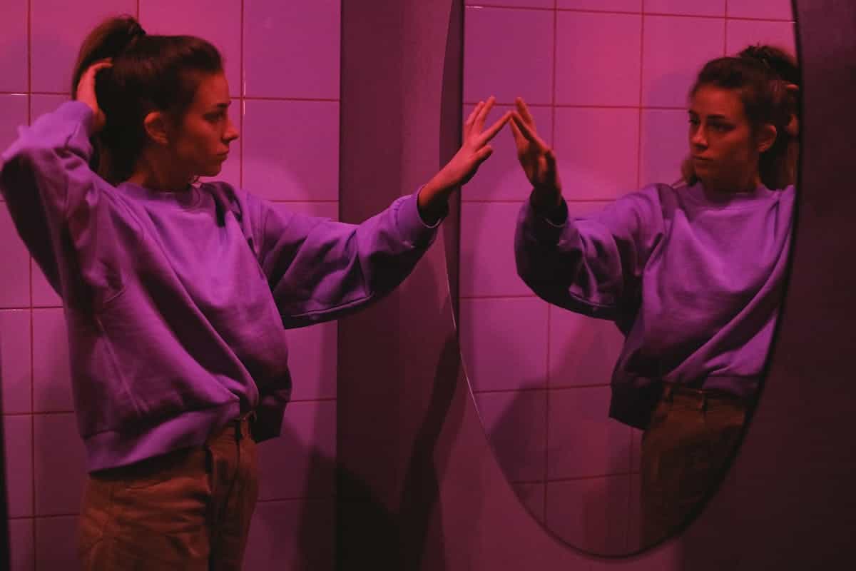 Pink-lit interior portrait studying reflection illustrating contemplative closure after exploring mirror portal symbolism