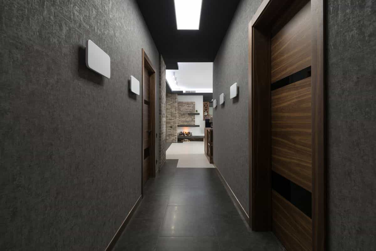 Long narrow corridor illustrating the far-end versus side-wall hallway mirror decision Long corridor with grey walls and doors leading to a bright room, illustrating the hallway mirror far-end question
