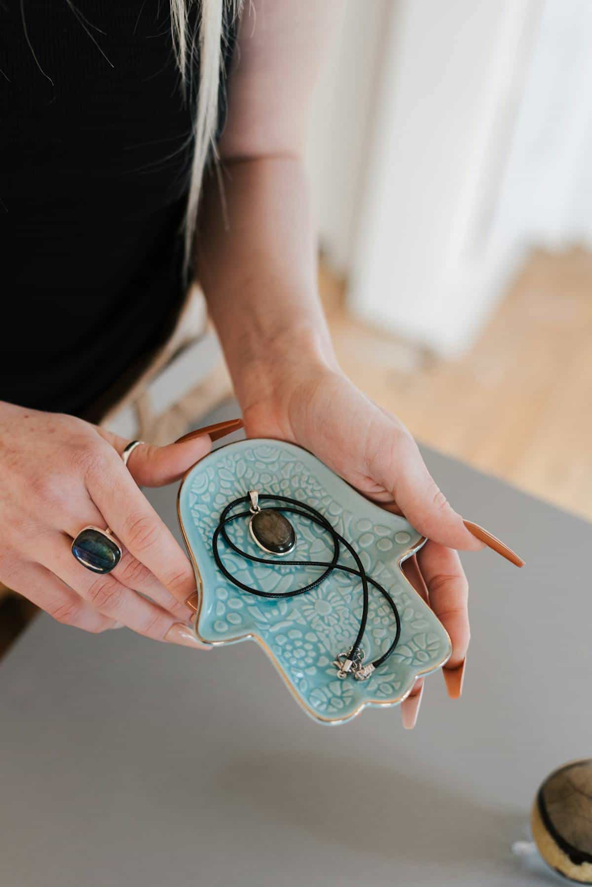 Anonymous person holding a decorative hamsa plate and small amulet showing protective hand symbolism