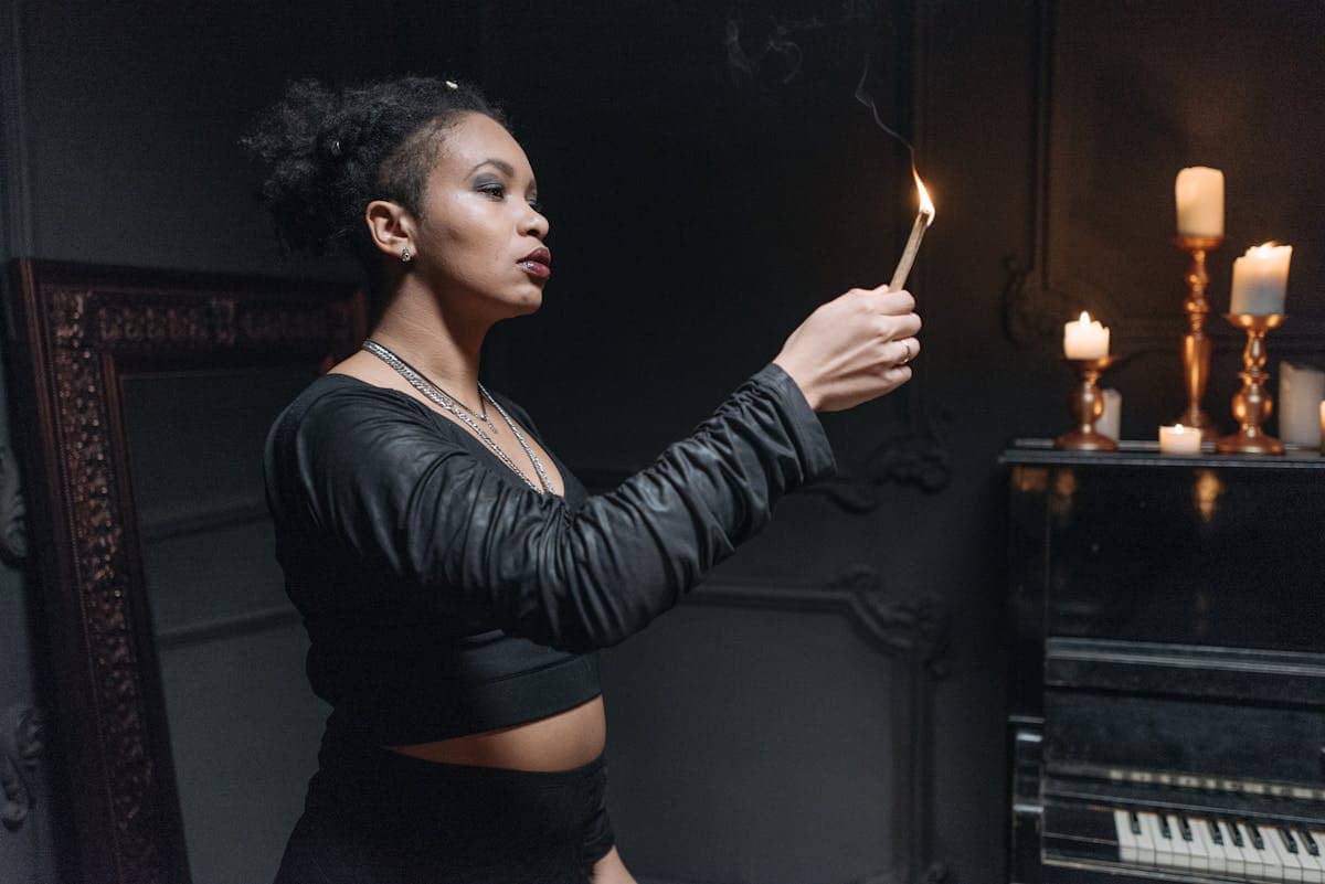 Woman holding a burning sage stick to cleanse a spiritual ritual object in a ceremonial setting