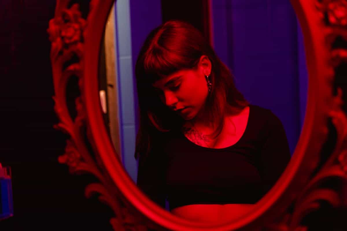 Woman reflected in a vintage mirror under dramatic red lighting creating an intense and mysterious mood