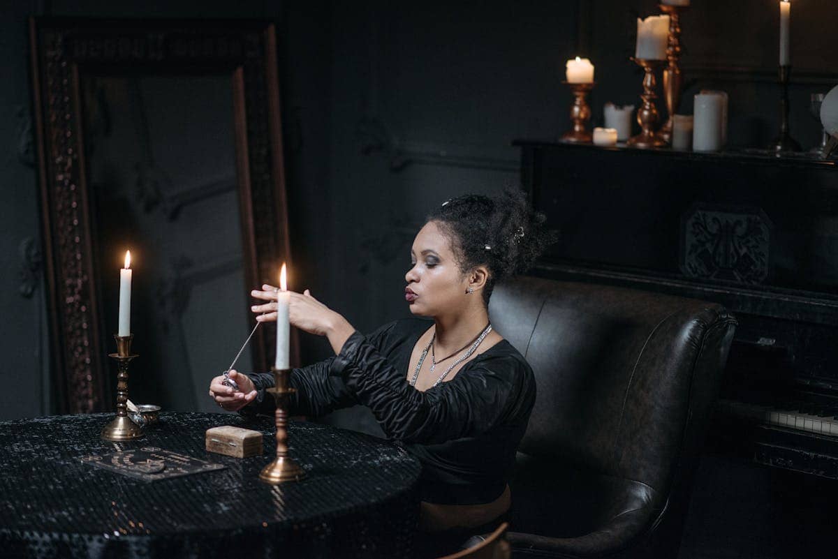 Woman meditating with a pendulum in candlelight for a divination session focused on scrying practice