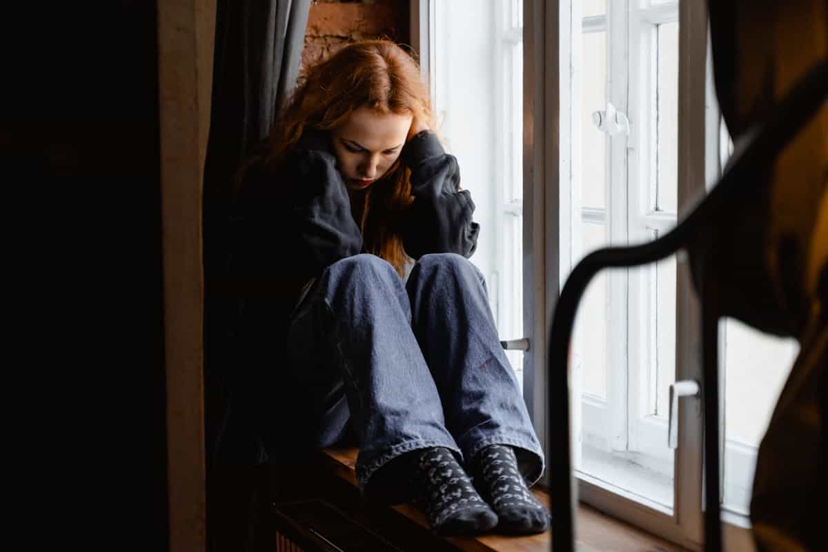 Woman sitting pensively by window representing mirror anxiety and the emotional impact of mirrors on mental health