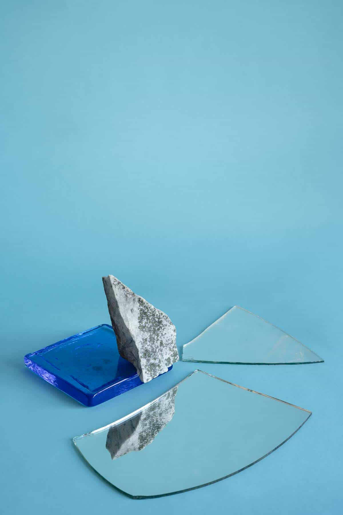 Minimalist broken mirror shards and stone on calm light blue tabletop