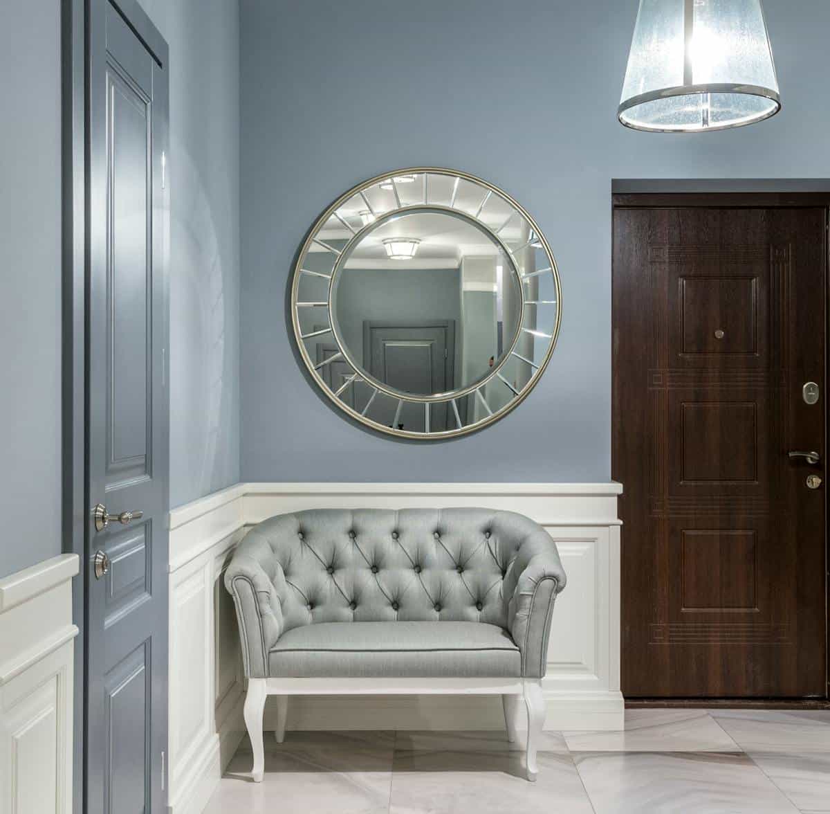 A modern and stylish hallway with a round mirror and tufted armchair, offering a welcoming ambience