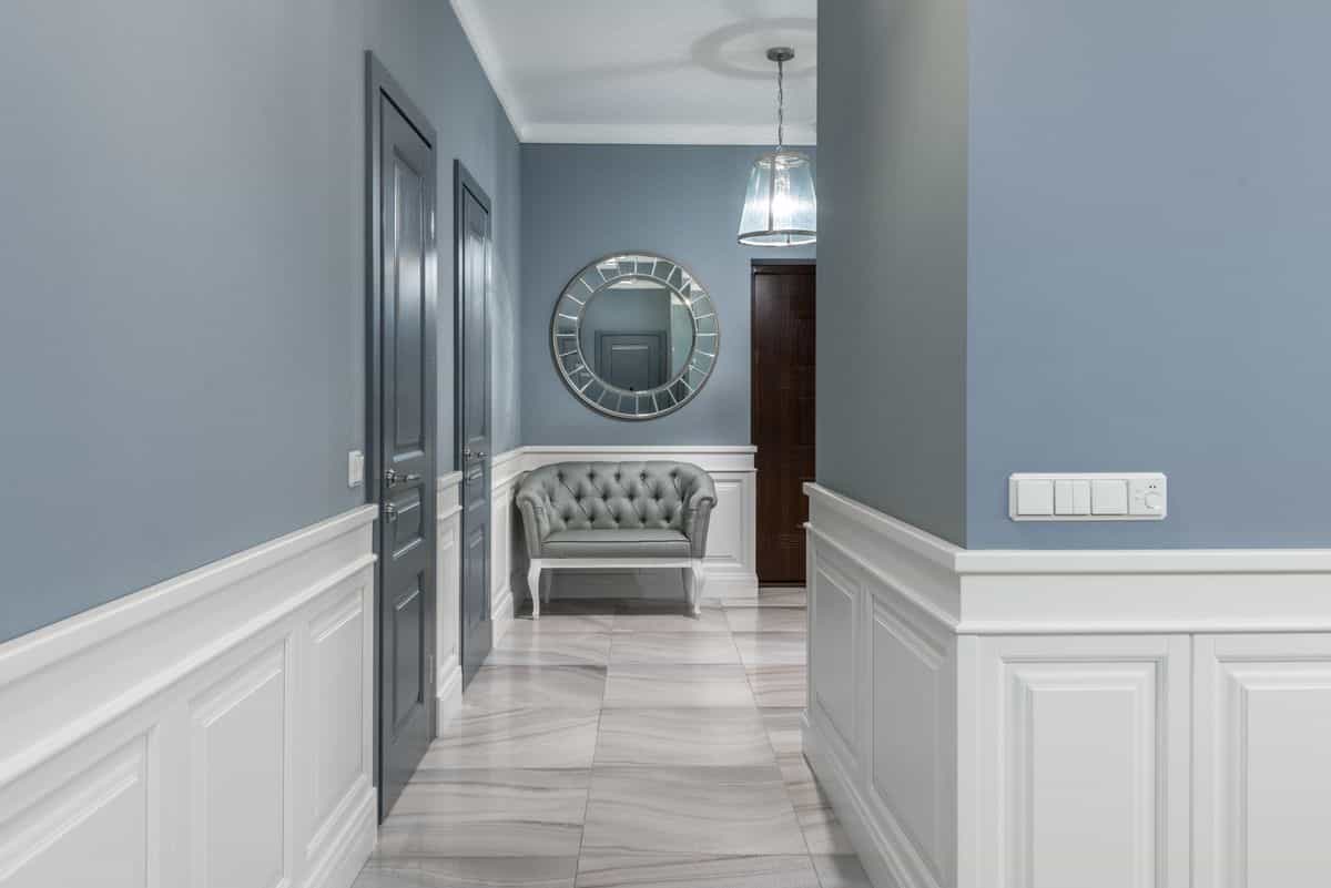 Narrow hallway with a decorative wall mirror and armchair, illustrating hallway mirror placement rules for narrow spaces.