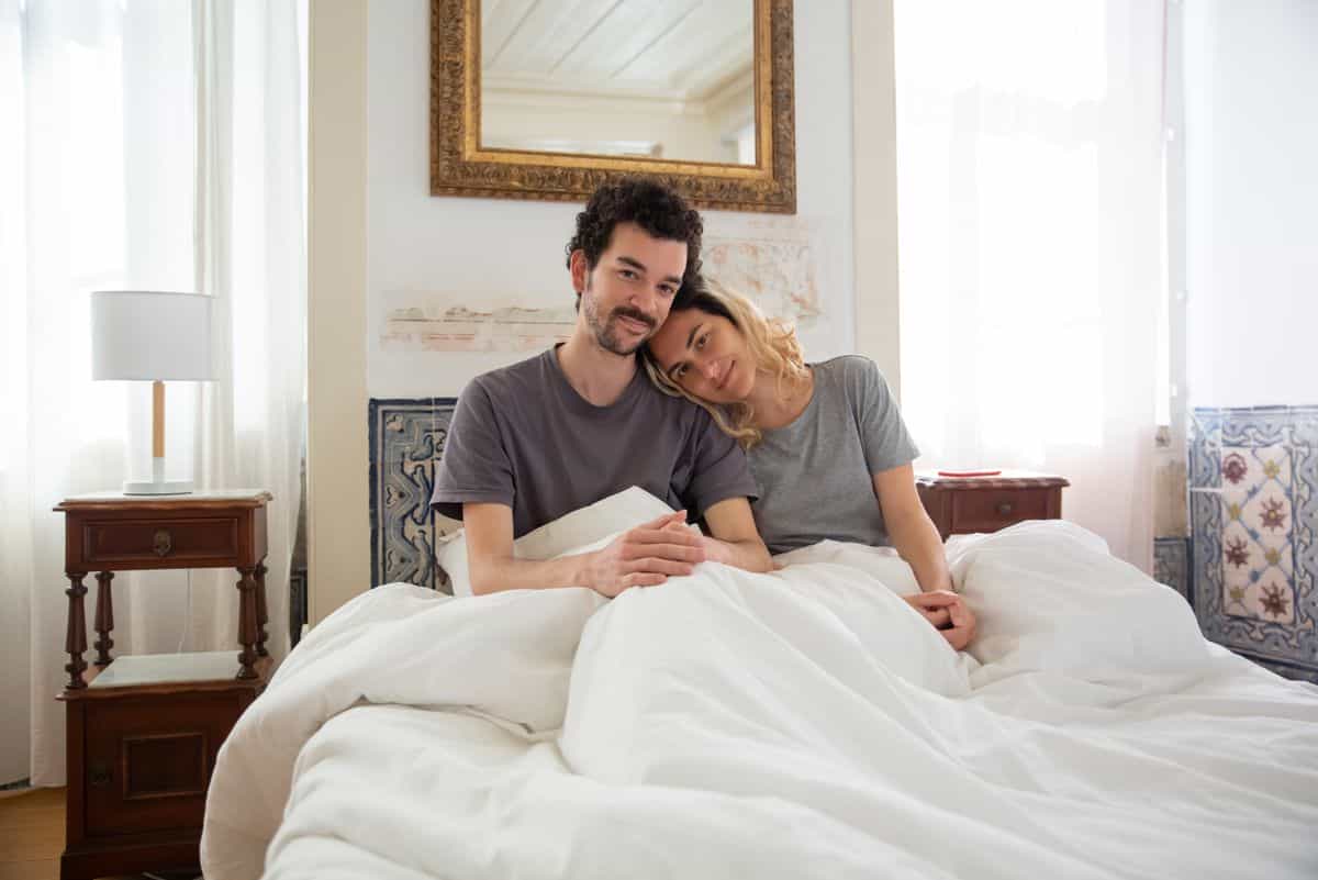 Couple in bed illustrating how to choose a shared feng shui sleeping direction Happy couple relaxing together in a bright, cozy bedroom, illustrating shared feng shui sleeping direction decisions