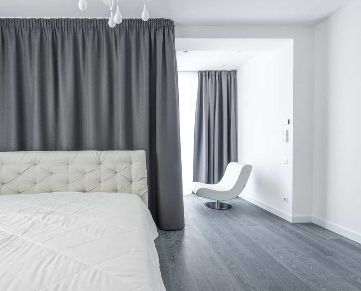 Bedroom in soft white and grey illustrating the Metal element in feng shui bedroom colors Modern bedroom with white bedding and soft grey curtains, illustrating the clarity of the feng shui Metal element